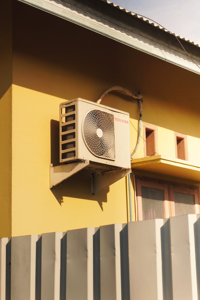 Outdoor air conditioner unit attached to a sunny yellow building facade.