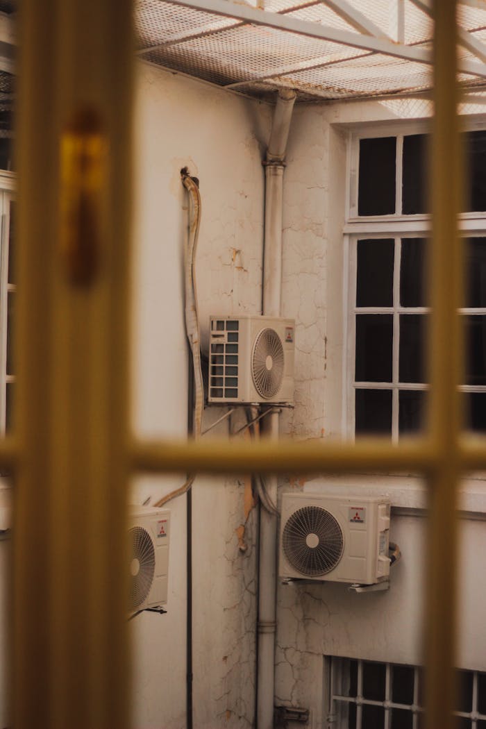 Air conditioners attached to the exterior of an old building, seen through a window.