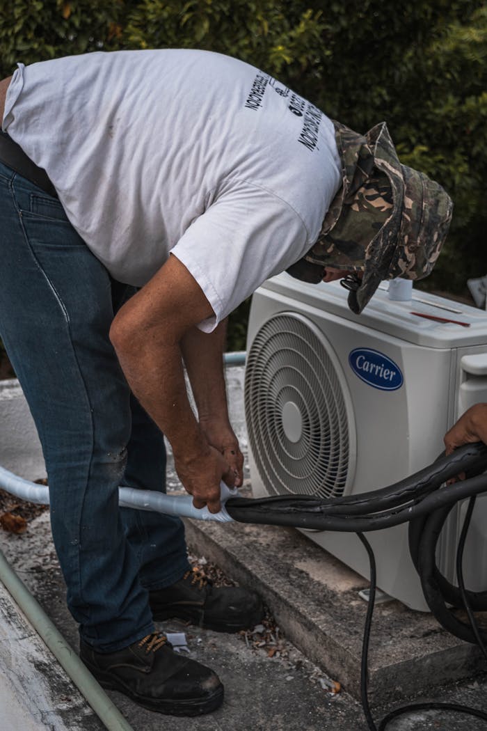 services-05 A technician performs maintenance on an outdoor air conditioning unit, focusing on hose connections.